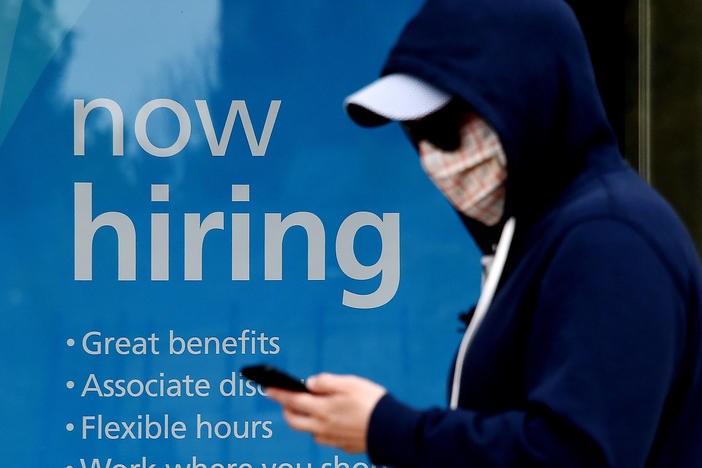 Millions of gig workers have come to depend on a government lifeline that's set to expire at the end of the year. Above, a man wearing a face mask walks past a sign saying "now hiring" on May 14 in Arlington, Va.