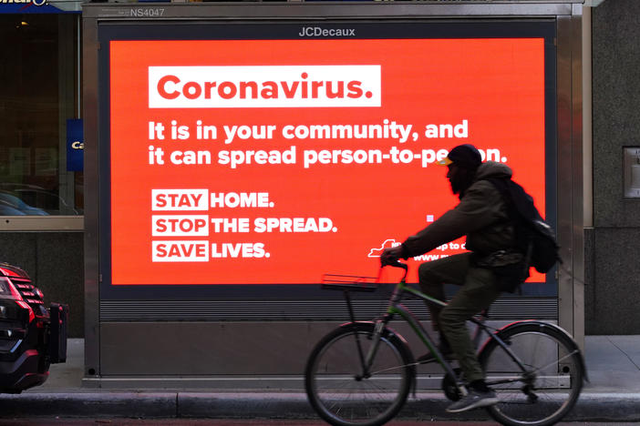 A person on a bike rides by a sign in New York City urging people to stay home in May. As the pandemic drags on, some workers are facing tough choices — balancing potential risks of unwittingly spreading the disease against the possibility of losing pay during a quarantine.