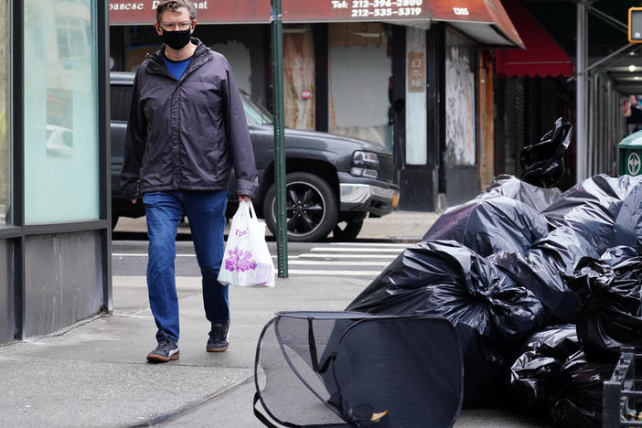 A man wearing a protective mask looks at piled-up trash in New York City on April 24. Cities are struggling with collection as the volume of residential garbage surges during the stay-at-home era.