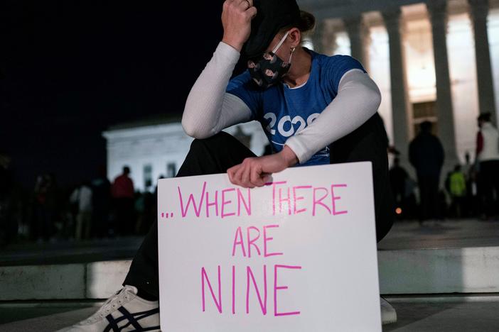 A woman, mourning the death of Ruth Bader Ginsburg, holds a sign at the Supreme Court that reads, "when there are nine," something Ginsburg said to describe when there'd be enough women on the court.