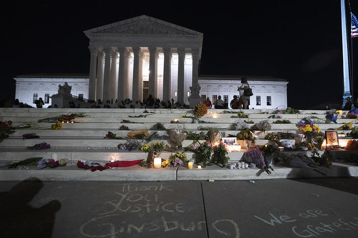 The national flag flies at half staff as people gather to mourn the passing of Supreme Court Justice Ruth Bader Ginsburg at the steps in front of the Supreme Court.