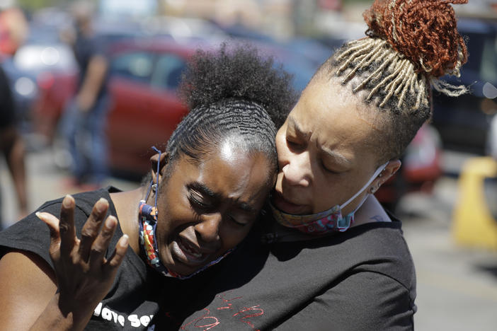 Two women pray in Louisville, Ky., in early June near the intersection where David McAtee was killed. Louisville police say video obtained from security cameras at McAtee's barbecue restaurant and an adjoining business show that McAtee fired a gun as police and National Guard soldiers were enforcing a curfew approached his business.