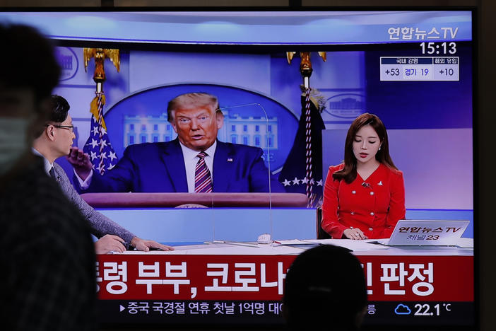 People pass a TV screen on Friday at the Seoul Railway Station. The Korean words on the screen say, "President Donald Trump and first lady Melania Trump tested positive for COVID-19."