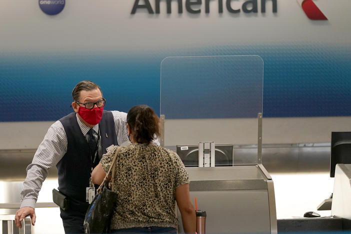 American Airlines ticket agent Henry Gemdron, left, works with a customer at Miami International Airport on Sept. 30. Travel industry groups warn of huge job losses if Congress and the White House fail to reach agreement on coronavirus relief soon.