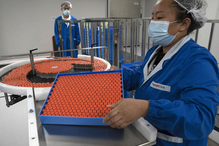 A worker feeds vials for production of a vaccine for COVID-19 at the SinoVac vaccine factory in Beijing. China said on Friday that it is joining the COVID-19 vaccine alliance known as COVAX.