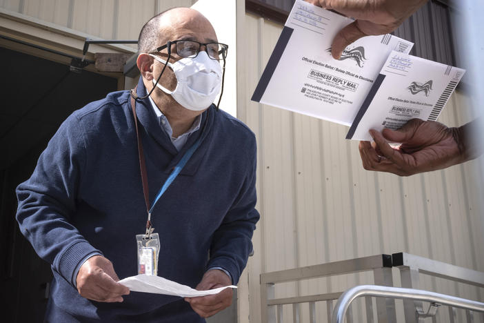 An employee of the Philadelphia City Commissioners Office examines ballot envelopes at a satellite election office at Overbrook High School in Philadelphia. Local election clerks can't start verifying mailed-in ballots in Pennsylvania until Election Day and in Michigan until the day before.