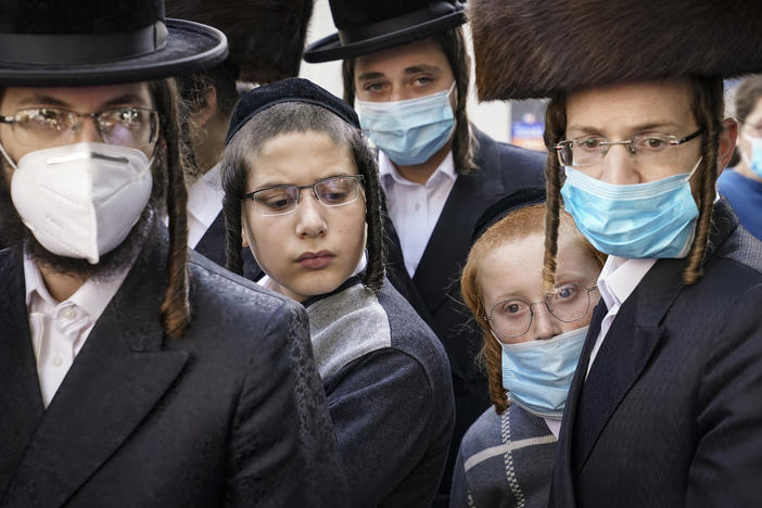 Members of the Orthodox Jewish community gather around a journalist as he conducts an interview on a street corner, last Wednesday, in the Borough Park neighborhood of the Brooklyn borough of New York. Gov. Andrew Cuomo moved to reinstate restrictions on businesses, houses of worship and schools in and near areas where coronavirus cases are spiking.