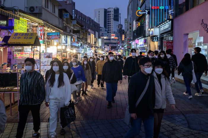 People wearing face masks walk on a street Sunday in the Hongdae district of Seoul, South Korea.