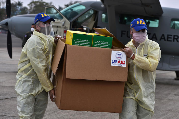 Foreign aid takes many forms — and Trump and Biden have differing perspectives. Above: Members of the Honduran Armed Forces carry a box of COVID-19 diagnostic testing kits donated by the United States Agency for International Development and the International Organization for Migration.