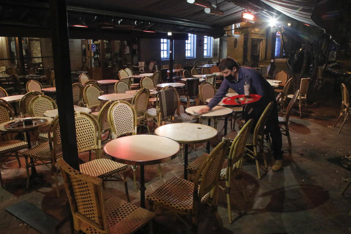 A waiter cleans a table this month after closing in St. Germain-en-Laye, west of Paris, to comply with COVID-19 restrictions forcing restaurants in the French capital to close. France has imposed a nighttime curfew in Paris and other major cities to curb the spread of the coronavirus.
