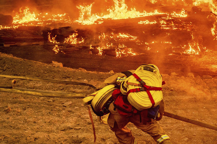 A firefighter carries a hose while battling the Glass Fire in a Calistoga, Calif., vineyard, Oct. 1
