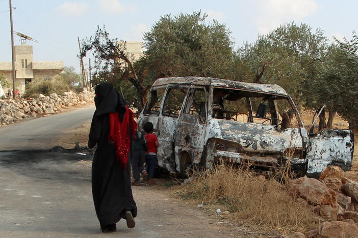 A woman walks past a wrecked van near the northwestern Syrian village of Barisha. Local residents and medical staff told NPR that noncombatant civilians who were in the van were injured and killed last year the night of the U.S. raid on the compound of ISIS leader Abu Bakr al-Baghdadi. The military says the men were combatants but found no weapons.