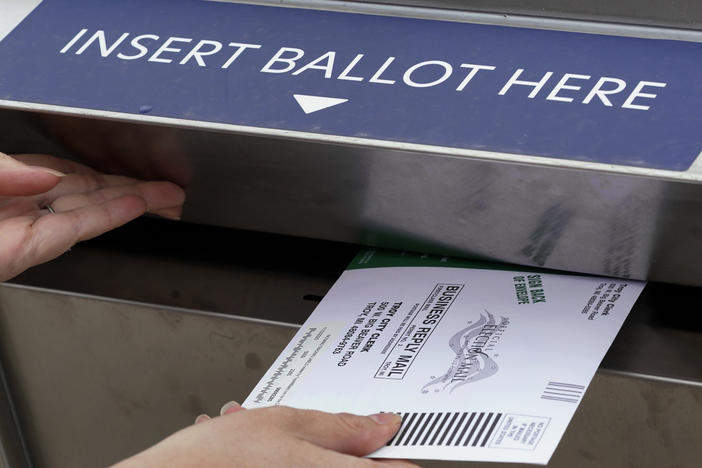 A voter is shown inserting her absentee voter ballot into a drop box earlier this month in Troy, Mich. A Michigan judge has blocked a ban on openly carrying guns in polling places on Election Day.