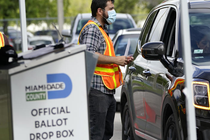 An election worker takes ballots from voters dropping them off at an official ballot drop box this week at the Miami-Dade County Board of Elections in Doral, Fla.