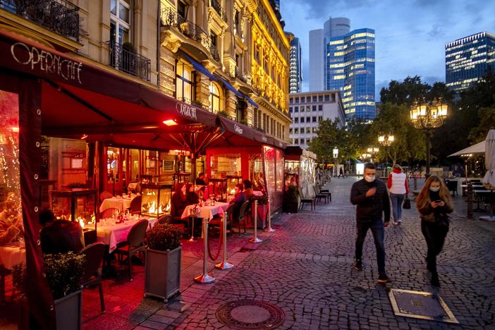 People wearing face masks walk past an outdoor restaurant Wednesday in Frankfurt, Germany. To slow the spread of the coronavirus, restaurants will be closed, starting Monday.