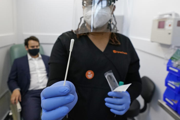 A medical assistant holds a swab after testing a man on Wednesday at the new COVID-19 testing facility at Boston Logan International Airport.
