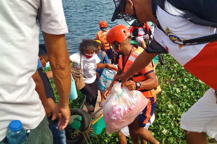 In this photo provided by the Philippine Coast Guard, families are evacuated by members of the Philippine Coast Guard to safer ground in Camarines Sur province as they prepare for typhoon Goni. Families living near coastal towns have moved to evacuation centers as the strong typhoon nears.