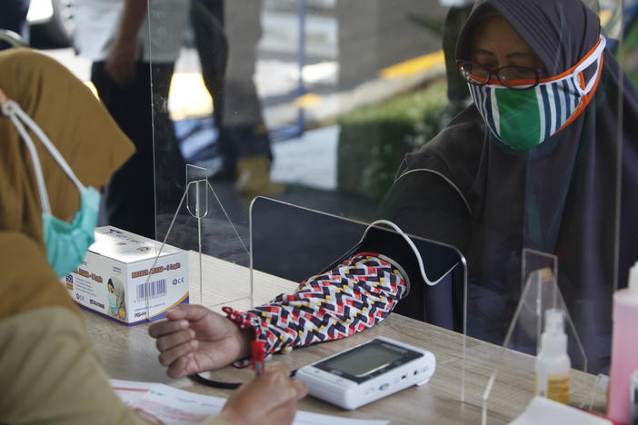 Health workers measure a woman's blood pressure during a simulation of a COVID-19 vaccine trial in Indonesia.