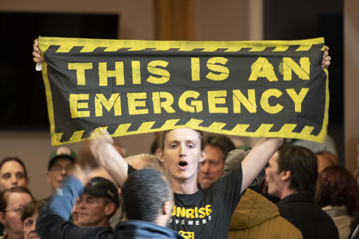 A climate change protester holds a banner reading, "This Is An Emergency," during a 2019 town hall event in Manchester, N.H., with Joe Biden, who isn't pictured.