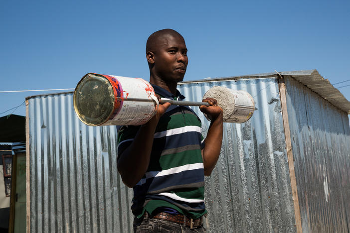 Alfred Sonandi plays around with a makeshift barbell — concrete poured into two tins on either end of a stick. People in the settlement of Covid don't usually wear masks: Living in such close quarters, they may (incorrectly) feel there's no point. They do mask up in public places where masking is mandatory.