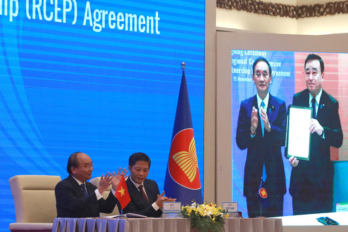 Vietnamese Prime Minister Nguyen Xuan Phuc (left) and Trade Minister Tran Tuan Anh applaud next to a screen showing Japanese Prime Minister Yoshihide Suga and Trade Minister Hiroshi Kajiyama holding up signed RCEP agreement, in Hanoi, Vietnam. China and 14 other countries have agreed to set up the trading bloc.