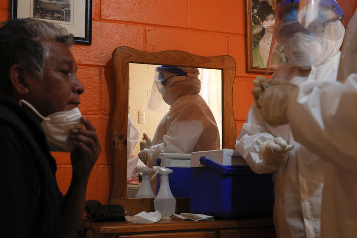 Ricardo Leon Luna, 74, lowers his mask as Doctors Delia Caudillo, right, and Monserrat Castaneda, prepare to take throat and nasal swabs as they conduct a COVID-19 test in his home in the Venustiano Carranza borough of Mexico City, on Thursday.
