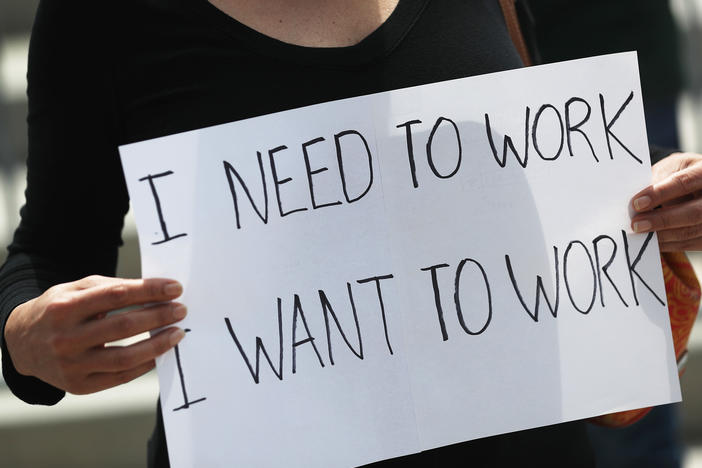 A protester holds a sign to protest measures in Miami to close indoor seating amid a rise in coronavirus cases. The number of unemployment claims rose for a second week, reinforcing concerns about the economy.