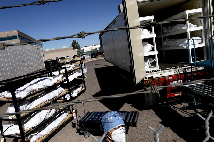 An inmate from the El Paso County detention facility prepares to load bodies wrapped in plastic into a refrigerated temporary morgue trailer.