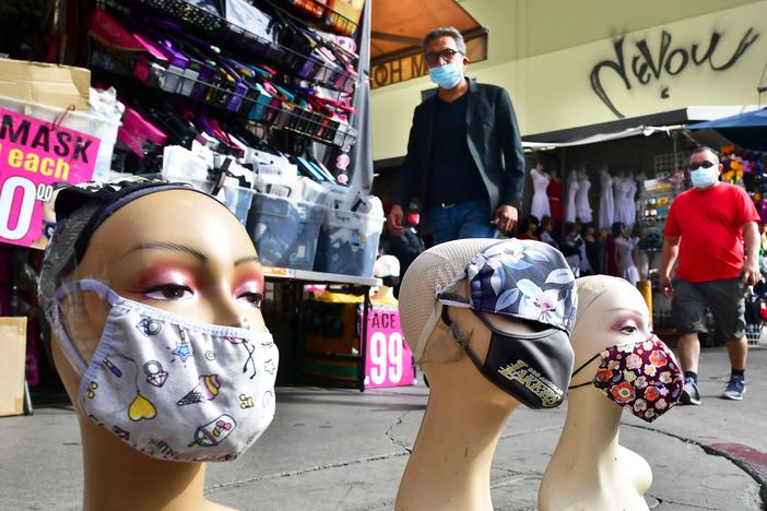 Pedestrians wearing masks walk past a display of mannequin heads also wearing masks this month in Los Angeles.
