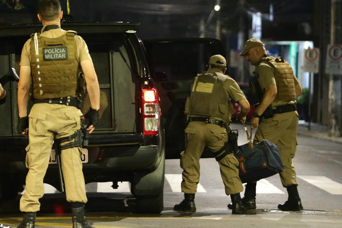 Military police officers carry a bag filled with money left behind by bank robbers in Criciúma, Santa Catarina state, Brazil, on Tuesday. Dozens of criminals armed with assault rifles invaded the city in southern Brazil overnight and took control of the streets as they assaulted a local bank.