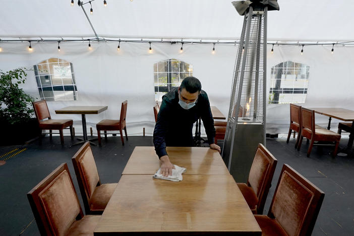 A person cleans a table in an outdoor tented dining area of a restaurant in Sacramento, Calif., on Nov. 19. Job growth slowed sharply in November as relief aid is due to expire at the end of the year.
