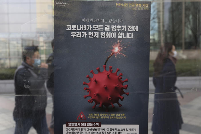 People wearing face masks as a precaution against the coronavirus pass by a poster emphasizing an enhanced social distancing campaign at a bus station on Monday in Seoul.