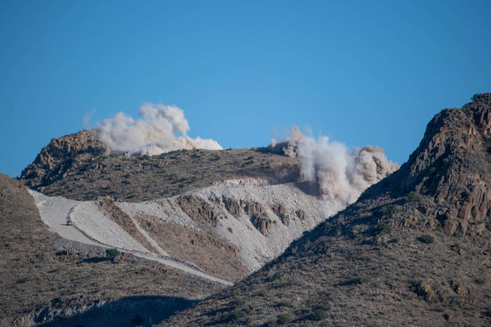 Dynamite raises clouds of dust above Guadalupe Canyon, near the New Mexico-Arizona border. The Diamond A Ranch, which is located next to the construction site, has sued the government, claiming the blasting has sent "car-sized boulders tumbling down onto ranch property."