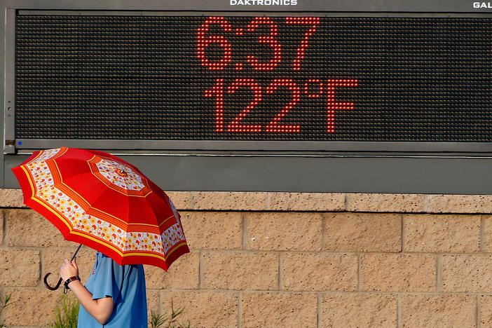 A pedestrian uses an umbrella to get some relief from the sun as they walk past a sign displaying the temperature on June 20, 2017 in Phoenix, Arizona. As 2020 comes to a close so does the hottest recorded decade.