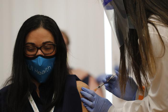 A doctor receives Chicago's first COVID-19 vaccination on Tuesday. In a new poll released the same day, respondents appeared to show less reluctance to receiving a coronavirus vaccine.