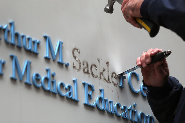 Tufts employee Gabe Ryan removes the Sackler family name from a building at Tufts University, the first major university to strip the Sackler name from buildings and programs.