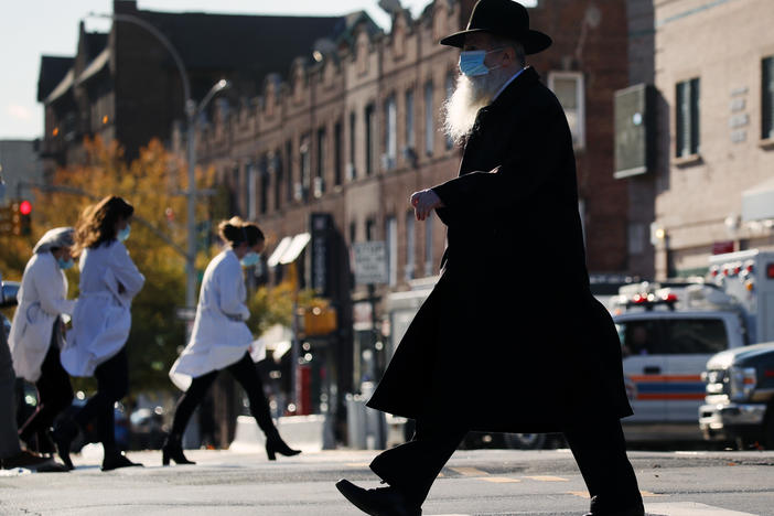 A Hasidic man and medical workers cross paths near the Maimonides Medical Center in Brooklyn, N.Y., in November. When public health messaging comes from community leaders, it's much more likely to be adopted, research on diverse groups finds.