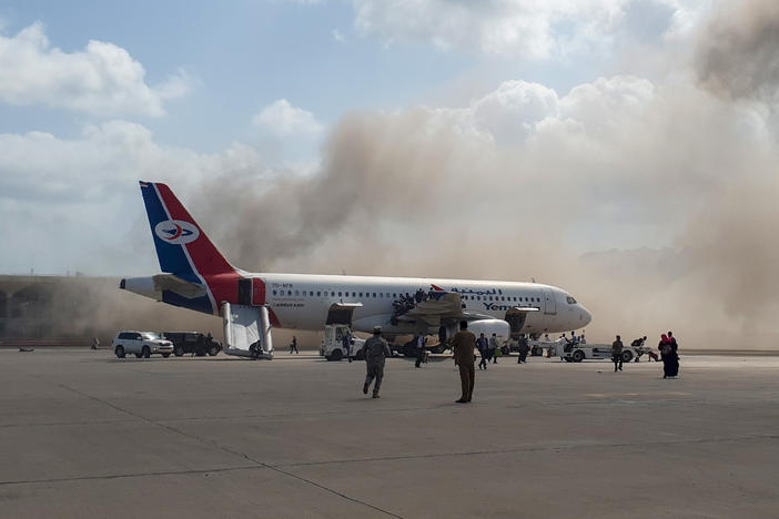 Smoke billows behind a plane that brought Yemen's new government to Aden International Airport on Wednesday. Explosions rocked the airport shortly after the plane arrived.