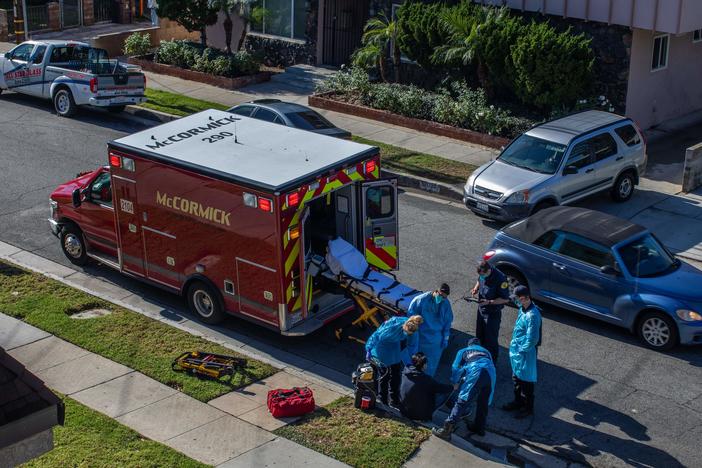 Los Angeles County paramedics examine a potential COVID-19 patient sitting on a curb before transporting him to a hospital in Hawthorne, Calif., on Dec. 29.