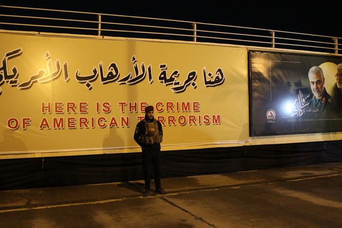 Iran is seeking to detain President Trump over the U.S. killing of top Iranian military commander Qassem Soleimani. Here, an Iraqi fighter stands in front of a banner at the site of the drone strike at Baghdad International Airport.