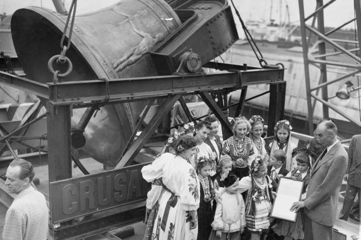 A group of former displaced persons helps load the Freedom Bell aboard a Navy transport vessel in Brooklyn, N.Y., on Oct. 9, 1950. One of the children, Eva Zandler, 8, originally from Poland, presents a scroll — to be enshrined in the Freedom Bell's tower in Berlin — to Frederick Osborn, the New York City chairman of the Crusade for Freedom.
