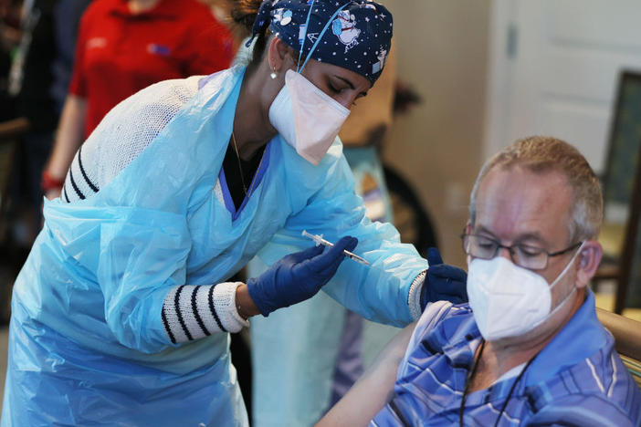 A health care worker with the Florida Department of Health administers a Pfizer-BioNtech COVID-19 vaccine at a retirement community in Pompano Beach, Fla. New Trump administration guidance arrived Tuesday, urging states to make all people over 65 eligible for the vaccine.