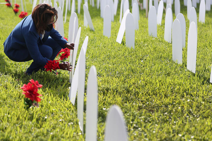 Mary Estime-Irvin, a councilwoman in North Miami, Fla., writes the name of a friend lost to COVID-19 on a symbolic tombstone that is part of a pandemic memorial at Griffing Park in North Miami in October.