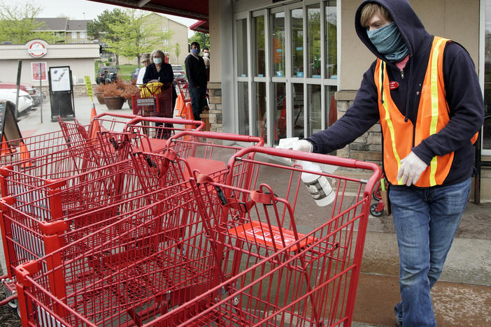 A Trader Joe's worker disinfects shopping carts and controls the number of customers allowed to shop at one time in Omaha, Neb., on May 7, 2020. Grocers like Trader Joe's are offering pay incentives to encourage their workers to get vaccinated against COVID-19.