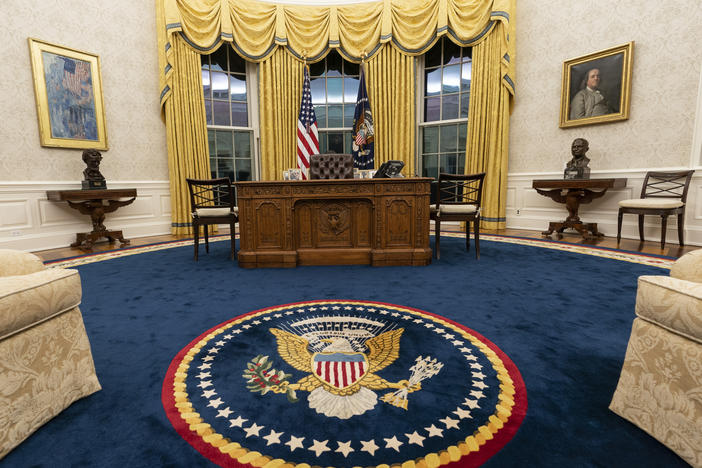 Biden kept the drapes and most of the furniture, but the rug and artwork in the Oval Office have changed. Flanking the Resolute desk are busts of Abraham Lincoln (left) and Harry Truman. Above Lincoln is <em>The Avenue in the Rain</em> by Childe Hassam. Above Truman is a portrait of Benjamin Franklin.