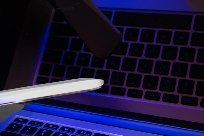 A handheld ultraviolet-C wand is waved over the surface of a computer keyboard.