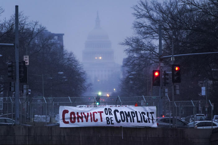 A sign reading "Convict or Be Complicit" hangs from a bridge on North Capitol Street in Washington, D.C., on the second day of former President Donald Trump's second impeachment trial.