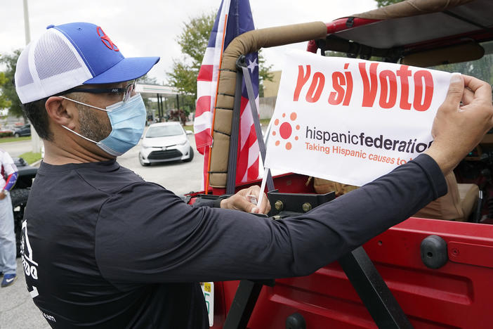 John Gimenez attaches a flag to his vehicle during an event hosted by the Hispanic Federation to encourage voting in the Latino community Sunday, Nov. 1, 2020, in Kissimmee, Fla. The Hispanic Federation is a non-partisan organization.