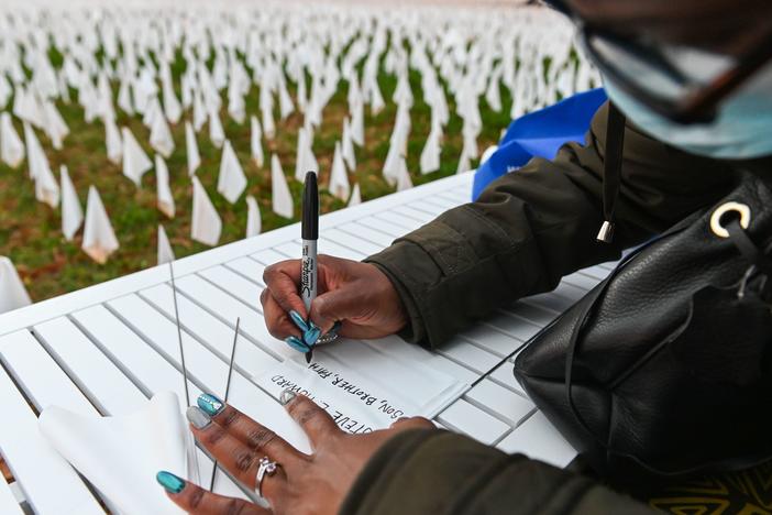 Patrice Howard writes on white flags before planting them to remember her recently deceased father and close friends in November at "IN AMERICA How Could This Happen...," a public art installation in Washington, D.C. Led by artist Suzanne Firstenberg, volunteers planted white flags in a field to symbolize each life lost to COVID-19 in the U.S.