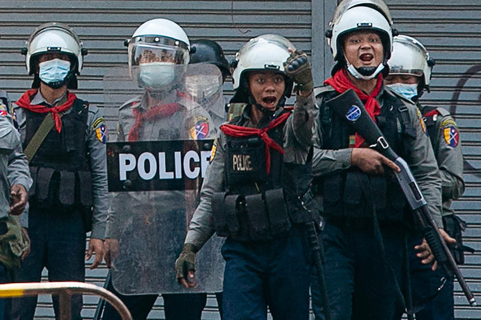 Police gesture toward protesters as security forces crack down on demonstrations against the military coup in Yangon on Sunday. The United Nations says at least 18 protesters were killed Sunday, the deadliest day yet since the military took power earlier this month.
